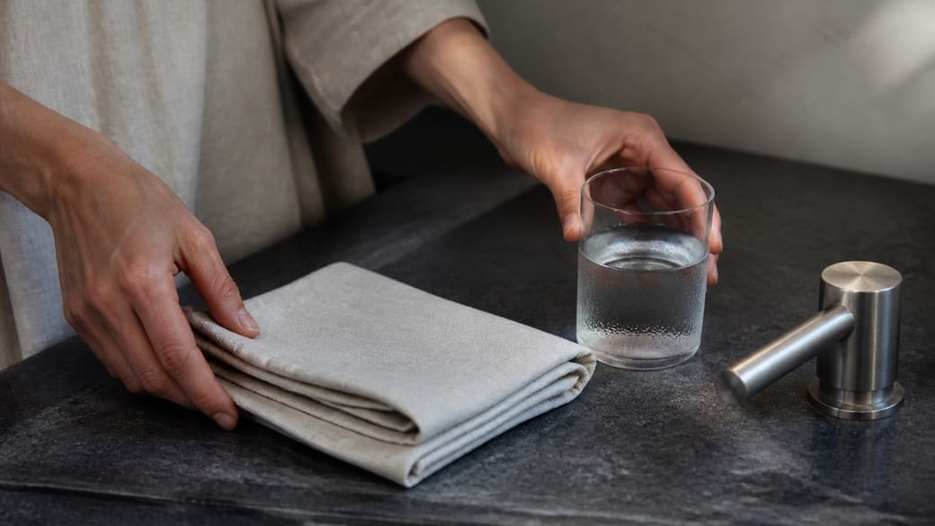 Mains préparant du lin et un verre d'eau sur une surface ardoise, sans appareil médical.